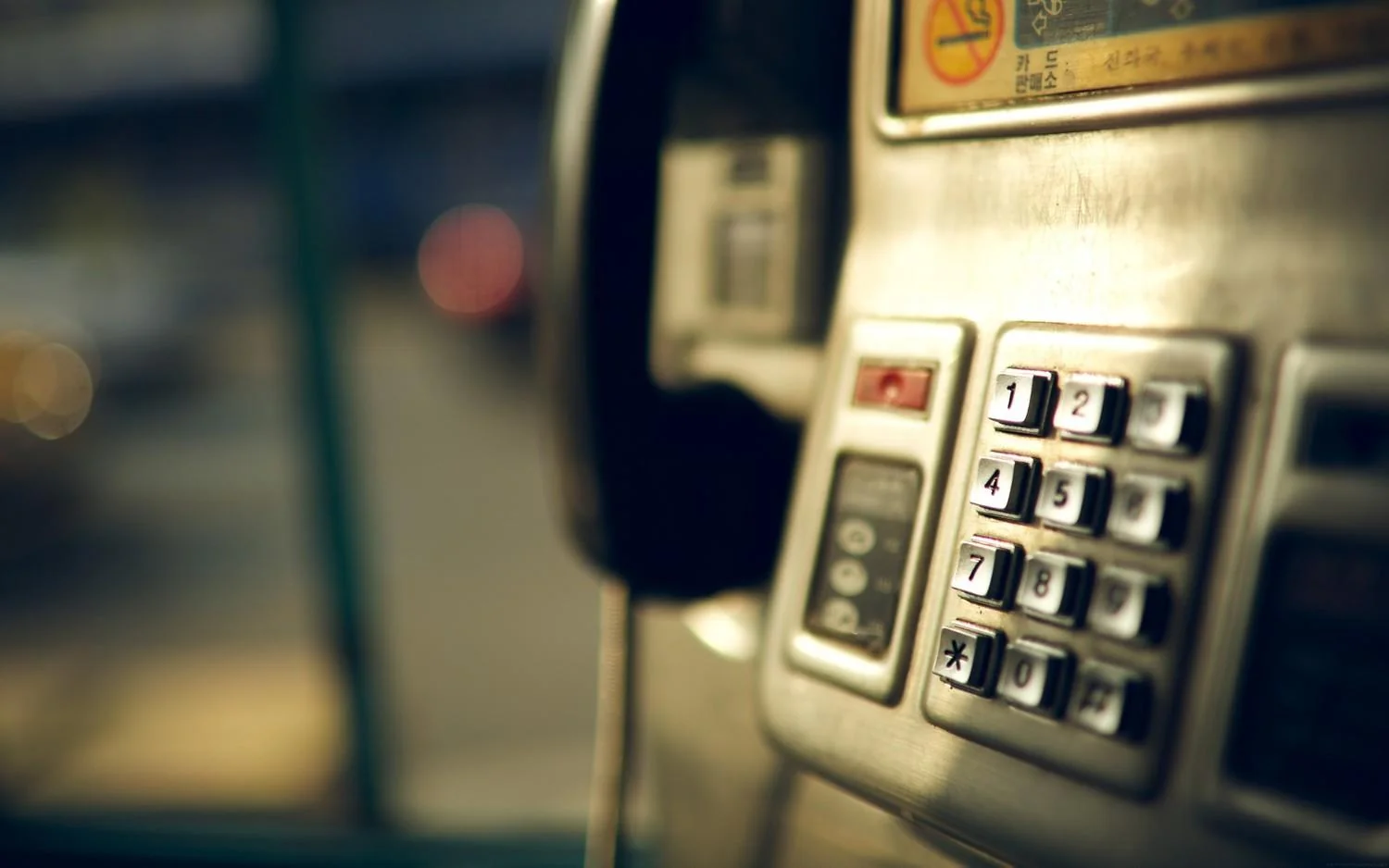 Close-up of a public telephone keypad and handset, lit warmly against a soft blurred background